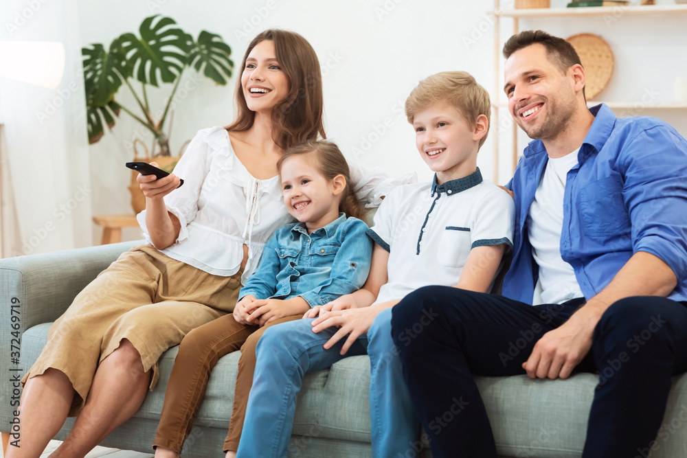 Family Of Four Watching TV Relaxing On Weekend At Home Family Of Four Watching TV Relaxing On Weekend At Home