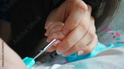 A newborn child's nails are cut with special baby scissors. An adult hand holds a small child's hand. Carefully, the mother cuts her daughter's nails. A child in a cocoon, home environment. Trust.