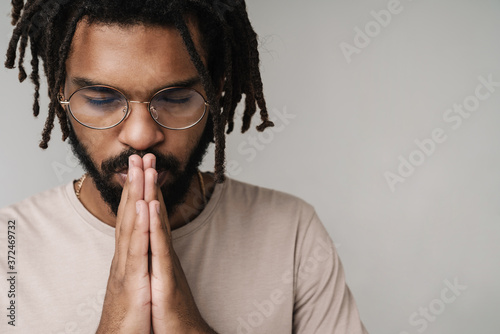 Praying african guy isolated over grey wall