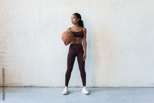 Photo of young african american sportswoman standing with basketball