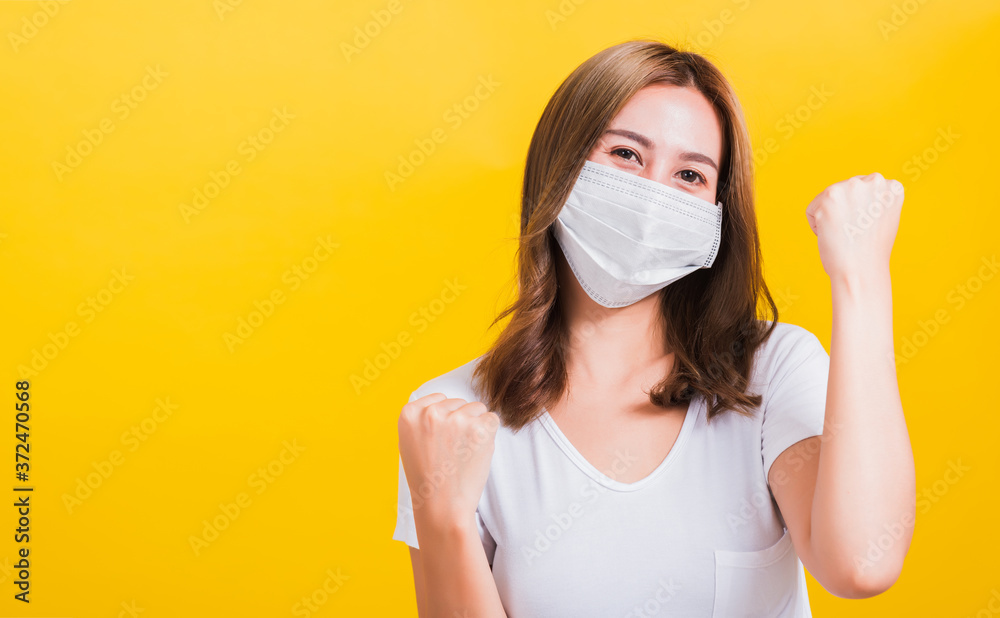 Asian beautiful happy young woman wearing face mask protection filter dust  pm2.5, COVID virus and air pollution her raise hands glad excited cheerful  after recovering from illness on yellow background foto de