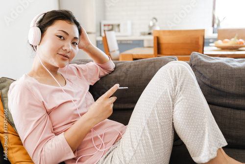 Smiling asian woman on couch listening to music at home