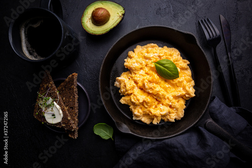 Fresh cooked scrambled eggs in a cast iron skillet on black background, top view