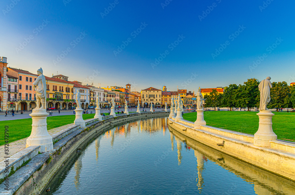Padua cityscape with statues near small canal on Piazza Prato della Valle square and row of colorful buildings in historical city centre, Padova town, Veneto Region, Italy
