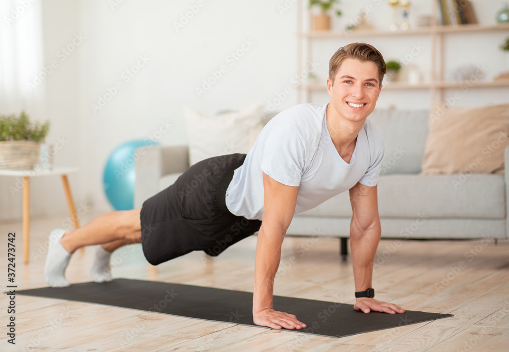 Keep fit and exercise at home. Smiling muscular guy doing push ups at mat in interior Keep fit and exercise at home. Smiling muscular guy doing push ups at mat in interior