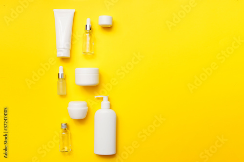 Cosmetics bottles on bright yellow background, top view, copy space. Mock up. White jars, bath accessories. Face and body care concept