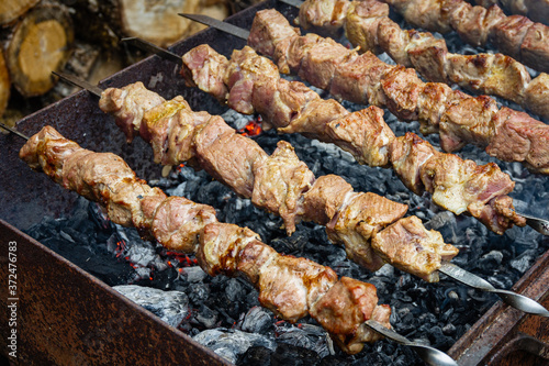 Traditional eastern dish, shish kebab. Grilled kebab cooking on metal skewer. Roasted meat cooked at barbecue. BBQ fresh beef meat chop slices. Grill on charcoal and flame, picnic, street food.