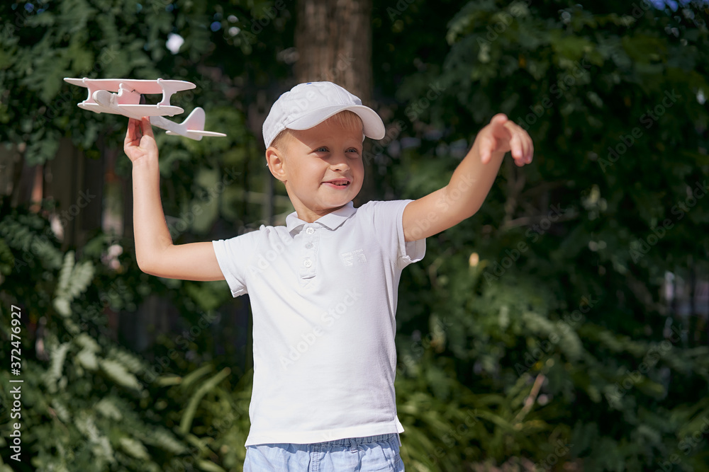 A boy in a cap launches a children's toy airplane in nature.