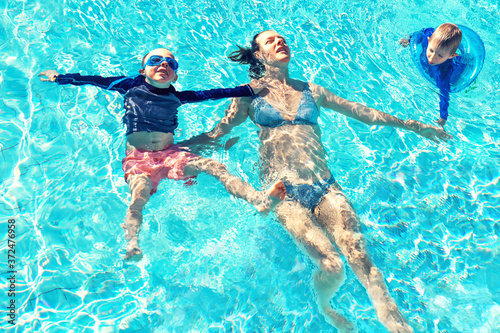 Mother and two little boys in swimming pool outside in sunny day, smiling face, enjoy in the water, close up portrait.