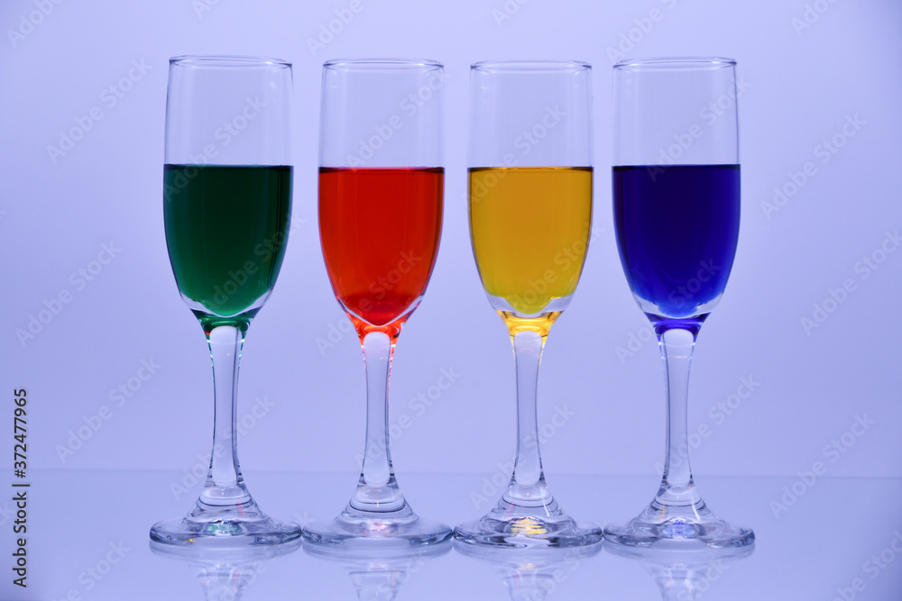 Flute glasses filled with green, red, yellow and blue liquid colors.
Flute glasses filled with green, red, yellow and blue liquid colors.