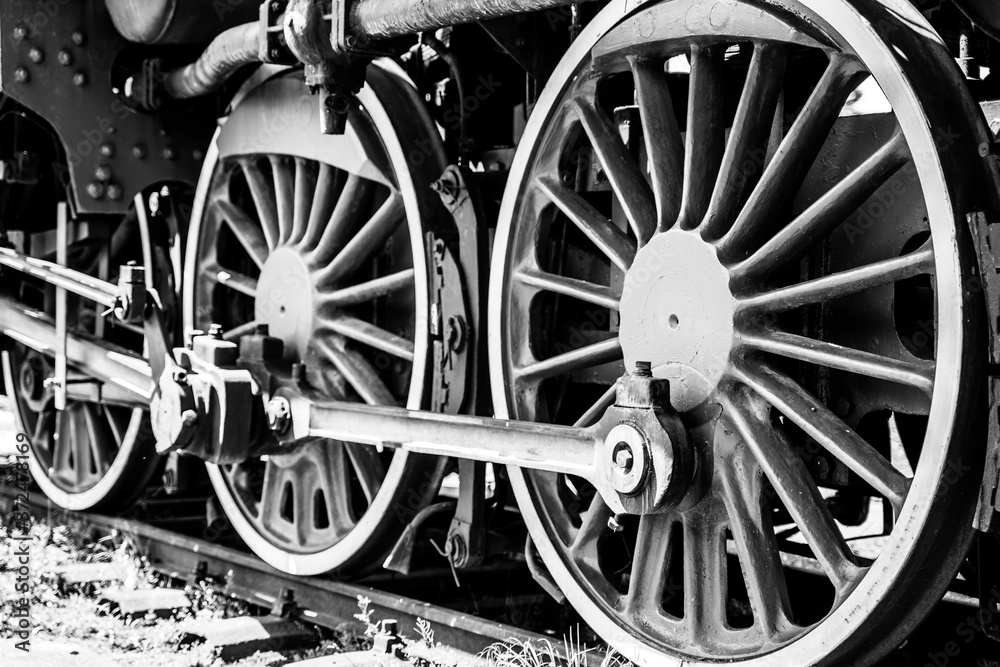 Fototapeta premium Huge vintage steam locomotive, red painted steel wheel detail close up. Coal-powered steam train stands on a siding. Classic gigantic heavy railway machinery. Side view of power parts of machine.