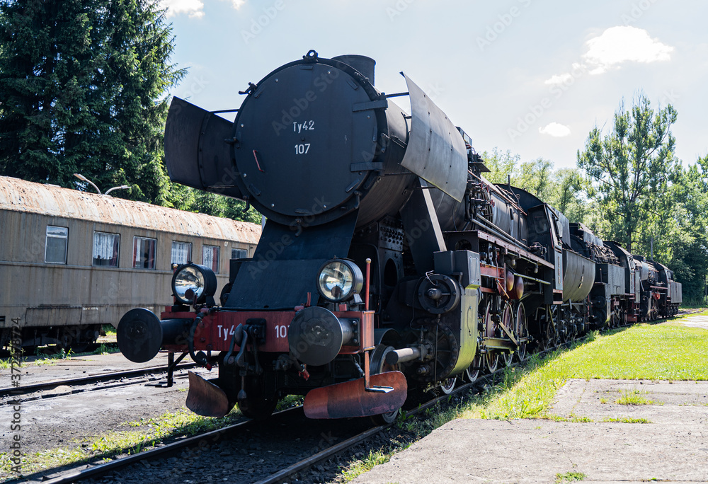 Fototapeta premium Huge vintage steam locomotive, red painted steel wheel detail close up. Coal-powered steam train stands on a siding. Classic gigantic heavy railway machinery. Side view of power parts of machine.