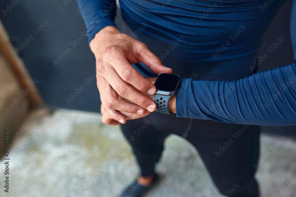 Closeup image of the athlete man in trendy sportswear looking to the smart watch before exercising outdoors. Fitness male  getting ready before running in the city street.