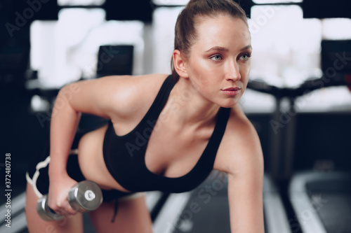 Young brunette sporty woman exercising with dumbbell in a gym