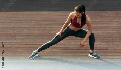 Full length shot of sporty woman stretching outdoor. Fitness girl doing some stretching exercises in the morning outside.