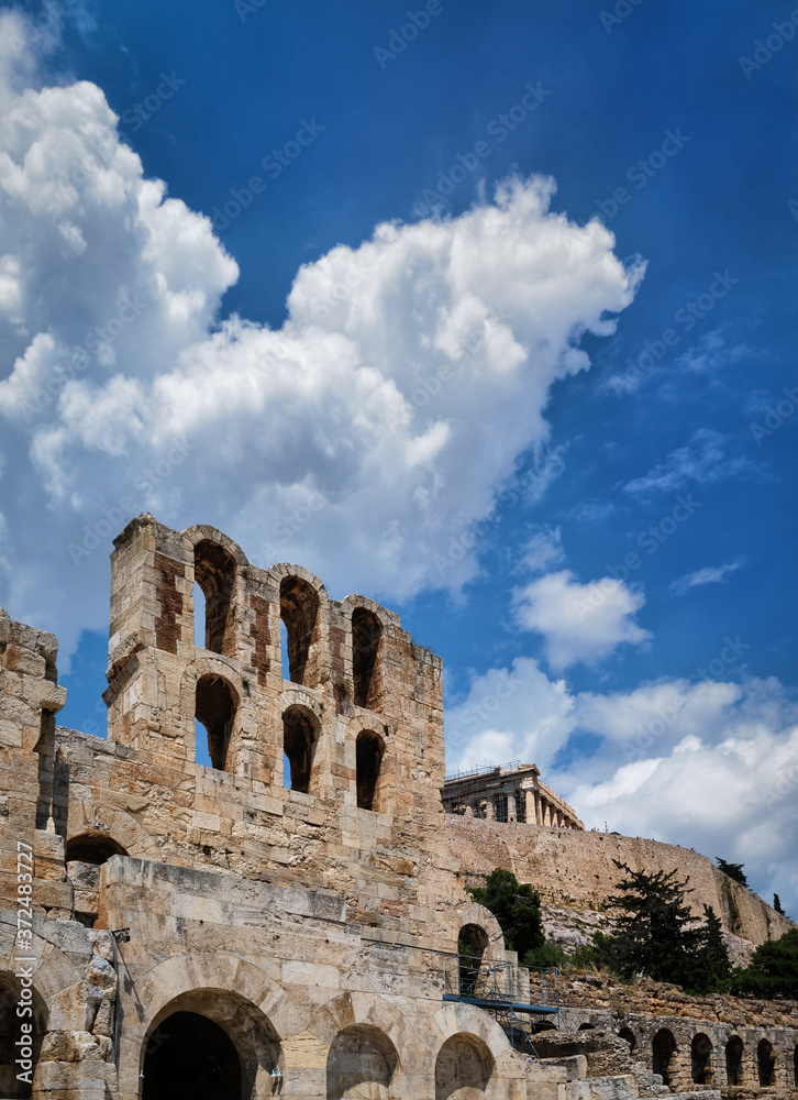 View of Odeon of Herodes Atticus theater on Acropolis hill, Athens, Greece, at bright blue sky and super clouds. Classic ancient Greek theater ruins
