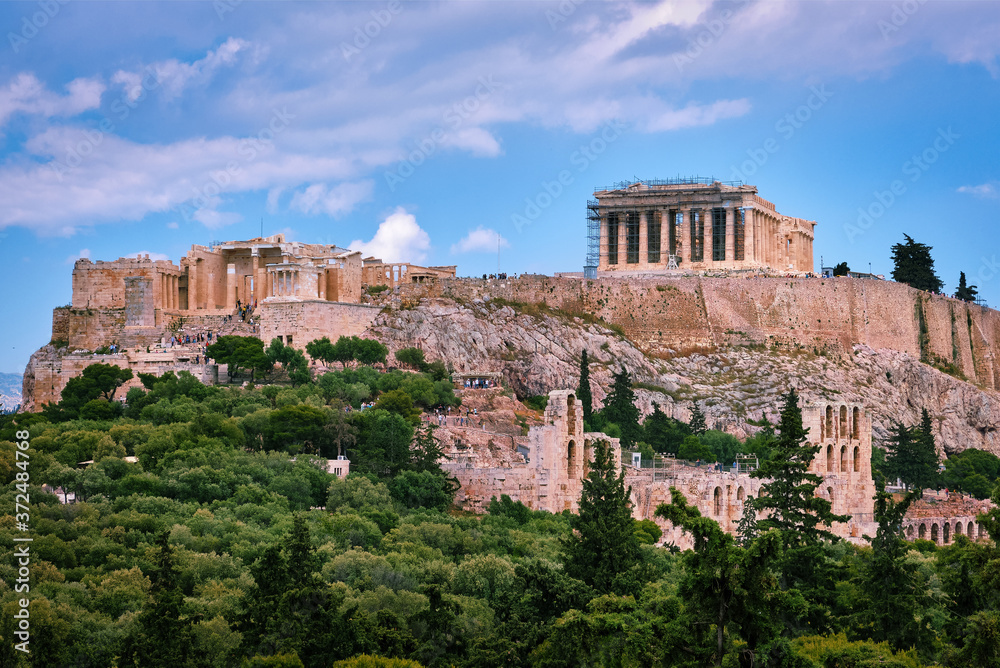 View of Acropolis hill and theater of Odeon in Athens, Greece from the hill of Philoppapos or Muses in summer daylight with great clouds in blue sky.
