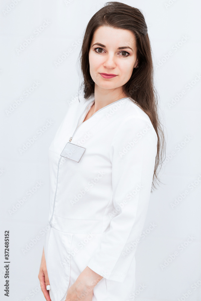 Serious brunette girl in a medical suit posing against a white wall background. The girl looks into the camera. Serious brunette girl in a medical suit posing against a white wall background. The girl looks into the camera.
