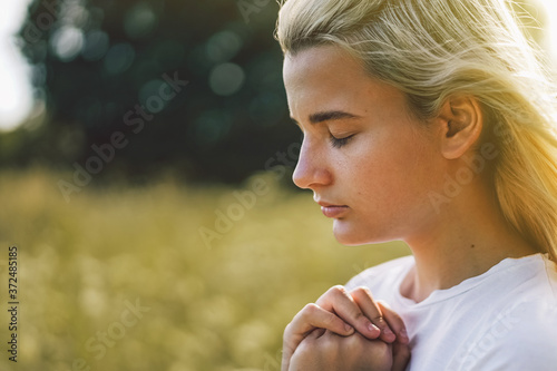 Girl closed her eyes, praying in a field. Hands folded in prayer concept for faith