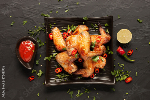 Roasted chicken, rosemary and chili-lime ketchup are prepared in an appetizing black plate ready to serve. Placed on the black table top view