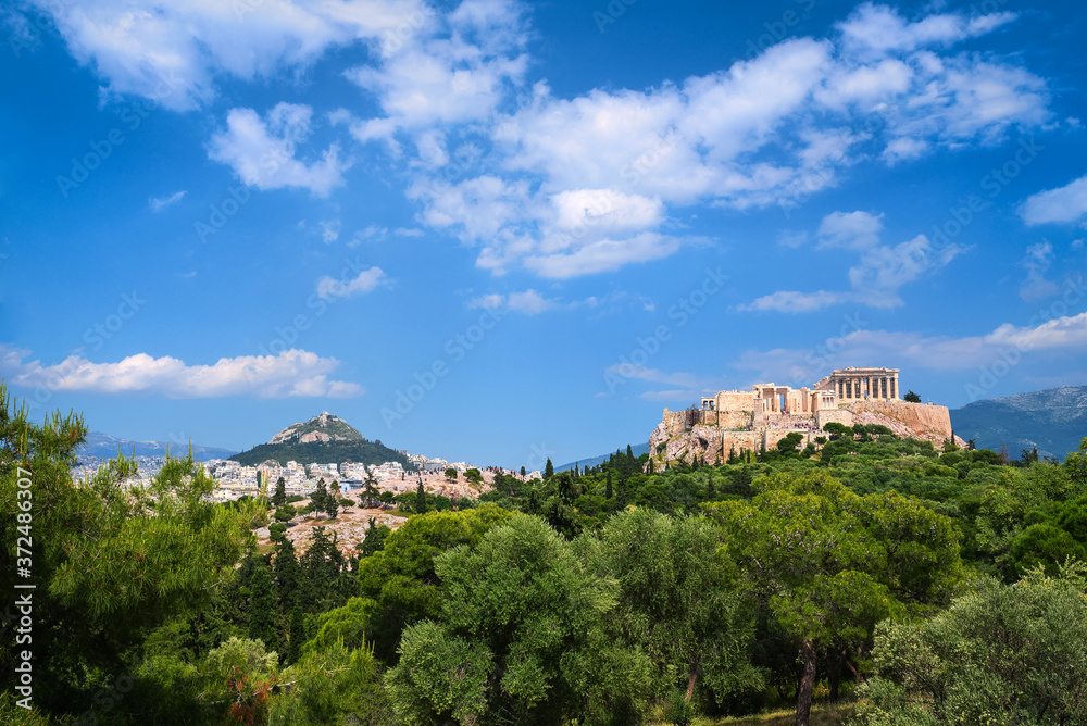 Iconic view of Acropolis hill and Lycabettus hill in background in Athens, Greece from Pnyx hill in summer daylight with great clouds in blue sky.