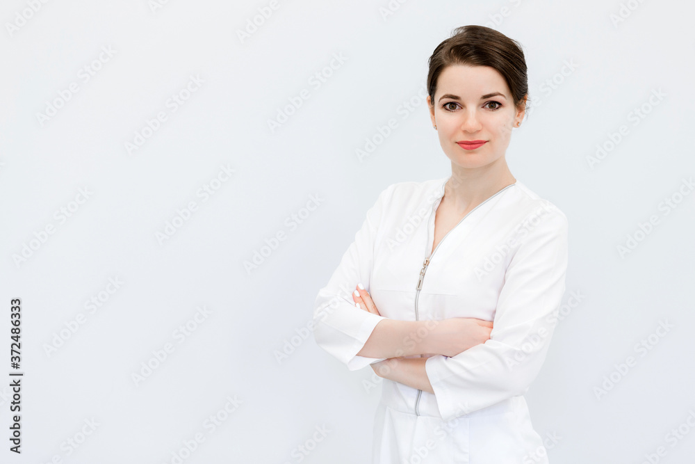 A beautiful and cute young woman with a bun hairstyle, a medical suit and crossed arms posing against a white wall. A beautiful and cute young woman with a bun hairstyle, a medical suit and crossed arms posing against a white wall.
