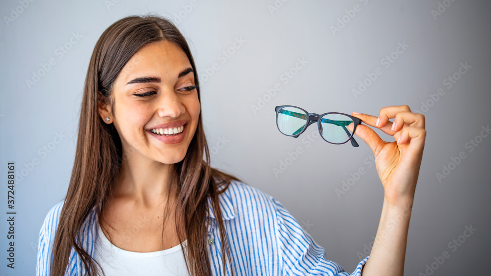 Smiling woman holding glasses and looking at camera isolated on a white background. Portrait of a smiling cute woman holding glasses over gray background. Smiling woman holding glasses and looking at camera isolated on a white background. Portrait of a smiling cute woman holding glasses over gray background.