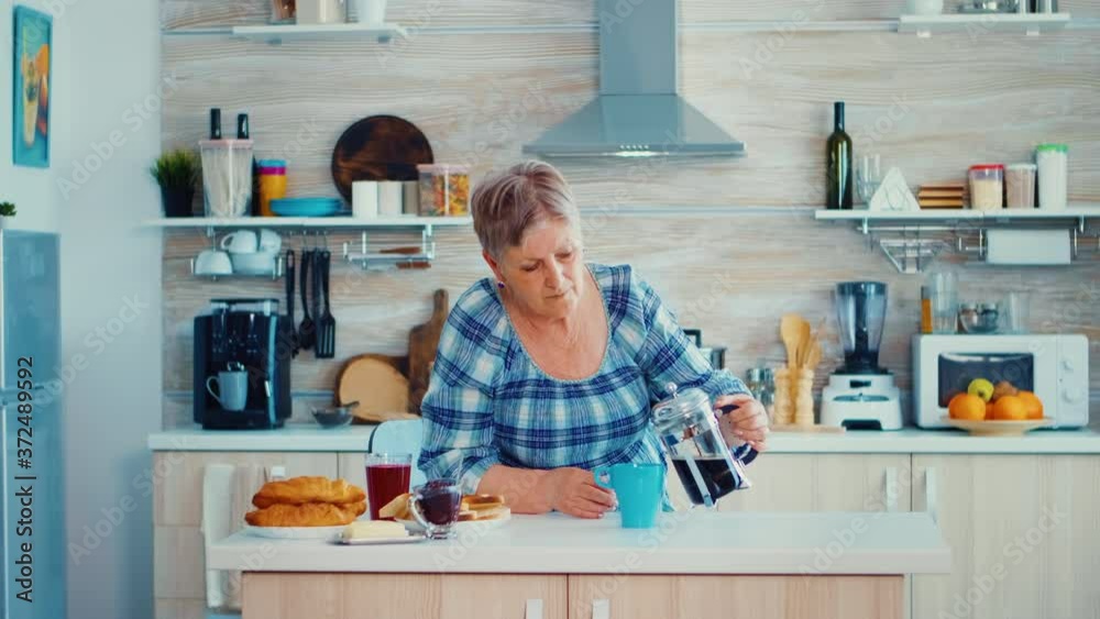 Mature woman in kitchen during breakfast pouring coffee from french press. Elderly person in the morning enjoying fresh brown cafe espresso cup caffeine from vintage mug, filter relax refreshment Mature woman in kitchen during breakfast pouring coffee from french press. Elderly person in the morning enjoying fresh brown cafe espresso cup caffeine from vintage mug, filter relax refreshment