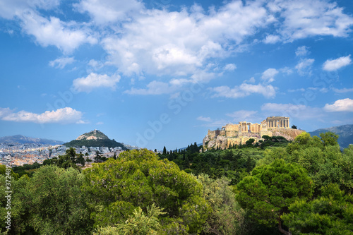 Iconic view of Acropolis hill and Lycabettus hill in background in Athens, Greece from Pnyx hill in summer daylight with great clouds in blue sky.