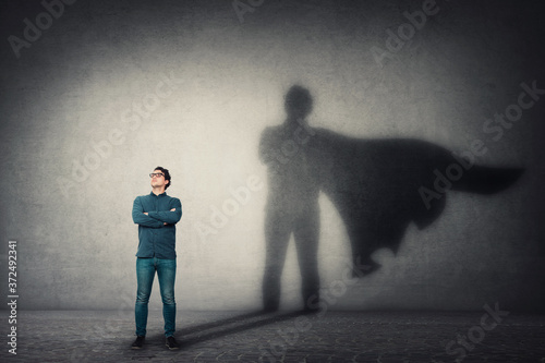 Fotografia Brave man keeps arms crossed, looks confident, casting a superhero with cape shadow on the wall