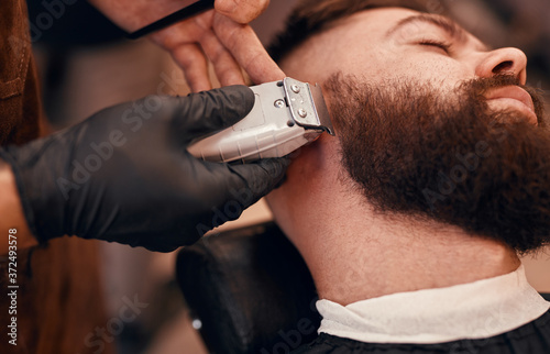 Crop barber trimming beard of hipster