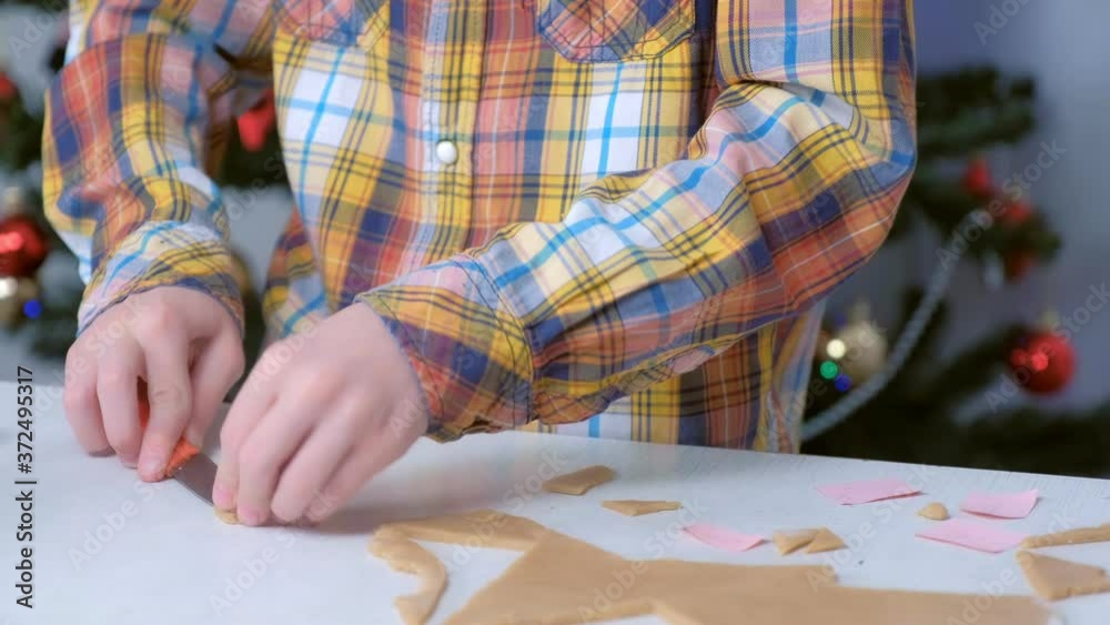 Boy is making gingerbread cookies from dough on Christmas tree background, hands closeup. Boy is using knife to cut cookies. Cooking baking cookies in New Year time. Sweet homemade bakery. Boy is making gingerbread cookies from dough on Christmas tree background, hands closeup. Boy is using knife to cut cookies. Cooking baking cookies in New Year time. Sweet homemade bakery.