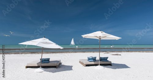 Panoramic view of a Caribbean beach a few meters from the Mexican Caribbean Ocean. Umbrellas and sunbeds on the beach. In the background  a catamaran sails off the coast of Holbox Island  Mexico