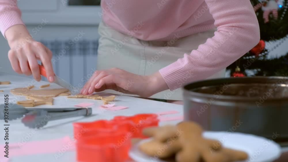 Woman is cutting parts for gingerbread house from dough and putting it in baking tray, hands closeup. Cooking baking cookies in New Year time. Sweet homemade bakery. Woman is cutting parts for gingerbread house from dough and putting it in baking tray, hands closeup. Cooking baking cookies in New Year time. Sweet homemade bakery.