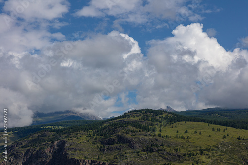a mountain valley with fields and rocks against a blue sky with thick white clouds. mountain Altai. the fjords in summer