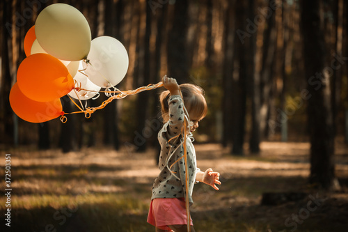 Cute little blonde girl holding balloons in the autumn forest. Birthday party outdoors