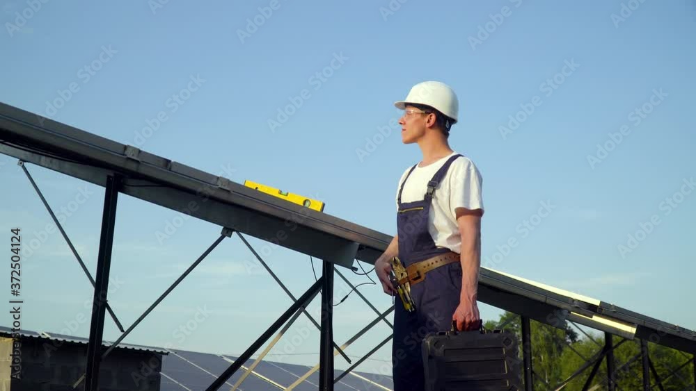 Young enginneer installing new sunny batteries. Worker in a uniform and hardhat installing photovoltaic panels on a solar farm Young enginneer installing new sunny batteries. Worker in a uniform and hardhat installing photovoltaic panels on a solar farm