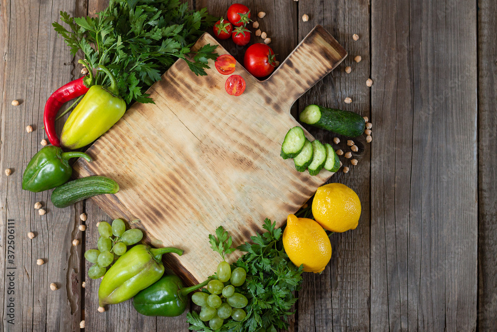 Wooden cutting board next to fresh herbs, raw vgetables and fruits on rustic wood table top view Wooden cutting board next to fresh herbs, raw vgetables and fruits on rustic wood table top view