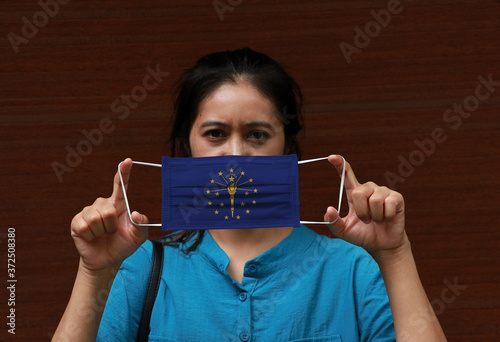 A woman and hygienic mask with Indiana flag pattern in her hand and raises it to cover her face. A mask is a very good protection from Tiny Particle or Covid 19. photo