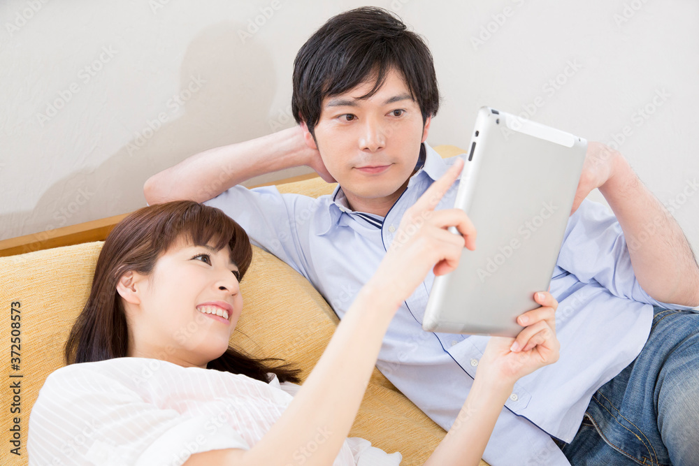 寝そべりながらタブレットPCを見る夫婦 寝そべりながらタブレットPCを見る夫婦