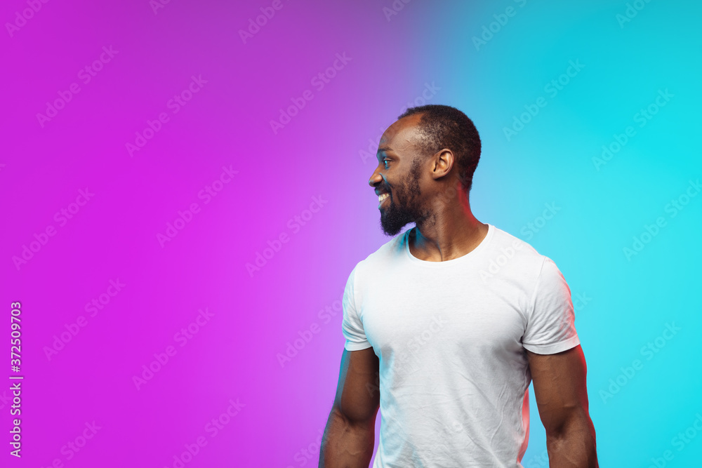 Smiling. African-american young man's portrait on gradient studio background in neon. Beautiful male model in casual style, white shirt. Concept of human emotions, facial expression, sales, ad. Smiling. African-american young man's portrait on gradient studio background in neon. Beautiful male model in casual style, white shirt. Concept of human emotions, facial expression, sales, ad.