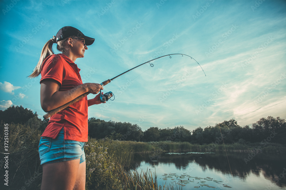 Cute caucasian woman is fishing with rod on the summer lake Stock