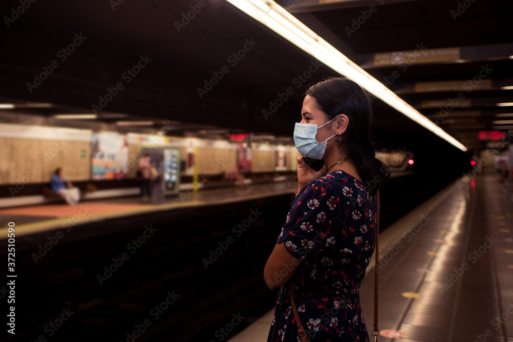 Young woman wearing face mask and talking with the mobile phone on the subway station. Concept of transportation on the new normal during coronavirus infection. Young woman wearing face mask and talking with the mobile phone on the subway station. Concept of transportation on the new normal during coronavirus infection.