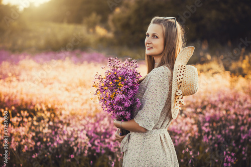 Obraz na płótnie Young woman with a bouquet of wildflowers standing on a sunny blooming meadow wi