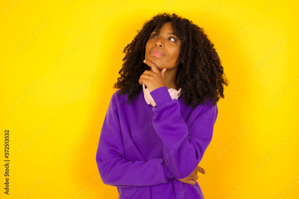 Portrait of thoughtful smiling girl keeps hand under chin, looks sideways, thinking or wondering about something with interest, dressed casually, poses against gray studio. Taking decisions concept. Portrait of thoughtful smiling girl keeps hand under chin, looks sideways, thinking or wondering about something with interest, dressed casually, poses against gray studio. Taking decisions concept.