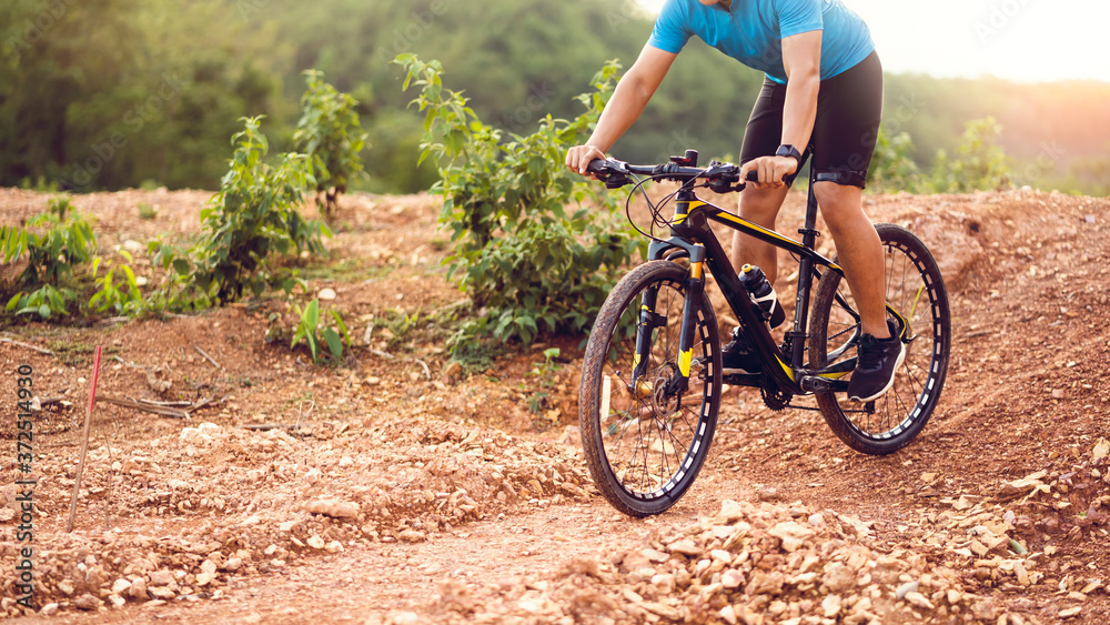 Fototapeta premium Close up mountain bikes cyclist cycling, Asian man athlete riding biking on rocky terrain trail, extreme sport wear gear uniform helmet, exciting freedom outdoor sunset nature healthy active lifestyle