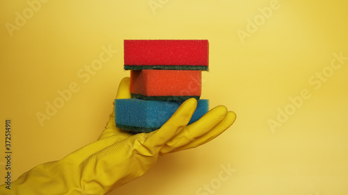 Hand in glove holding few washing sponges on yellow background - amount of housework concept