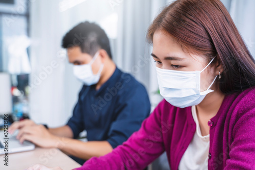 New normal asian couple wearing facemask working from home using tablet laptop computer online internet technology lifestyle, modern living room self isolation quarantine coronavirus COVID-19 pandemic