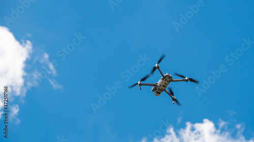 A drone hoving with blue sky and white puffy clouds above it.