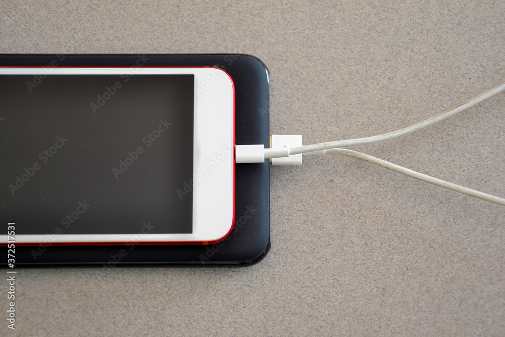 Smartphone connected to a power bank. Way to charge the battery of a mobile phone without connecting to electricity. Tools for telecommunting Smartphone connected to a power bank. Way to charge the battery of a mobile phone without connecting to electricity. Tools for telecommunting